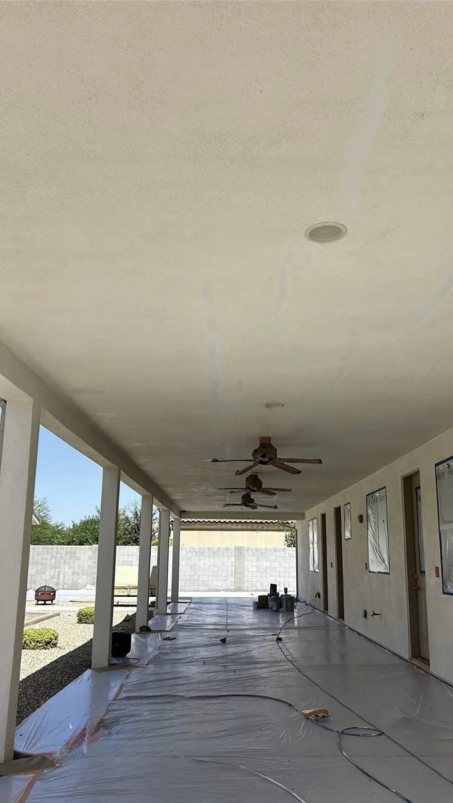 Covered patio ceiling in Peoria, Arizona mid-repaint, with the floor masked in plastic to protect it